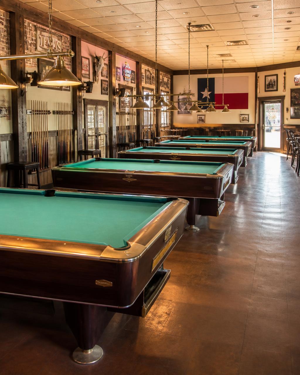 Rows of pool tables and cue racks inside a Texas billiards hall